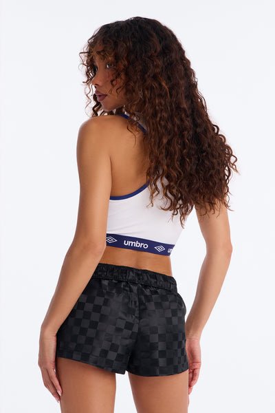 Woman wearing a white sports bra with Umbro logo and black checkered shorts on a white background