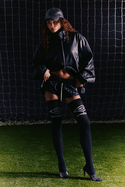 Person wearing a dark outfit with Umbro logo on a sports field