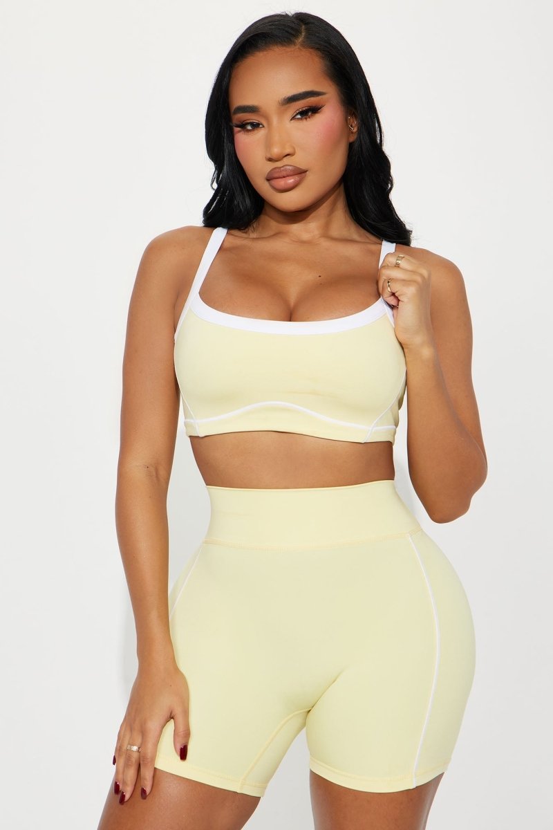 Woman wearing a light yellow sports bra and shorts set on a white background